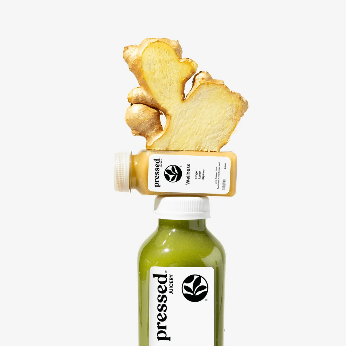 Bottle of pressed Wellness juice with a piece of ginger on top against a white background