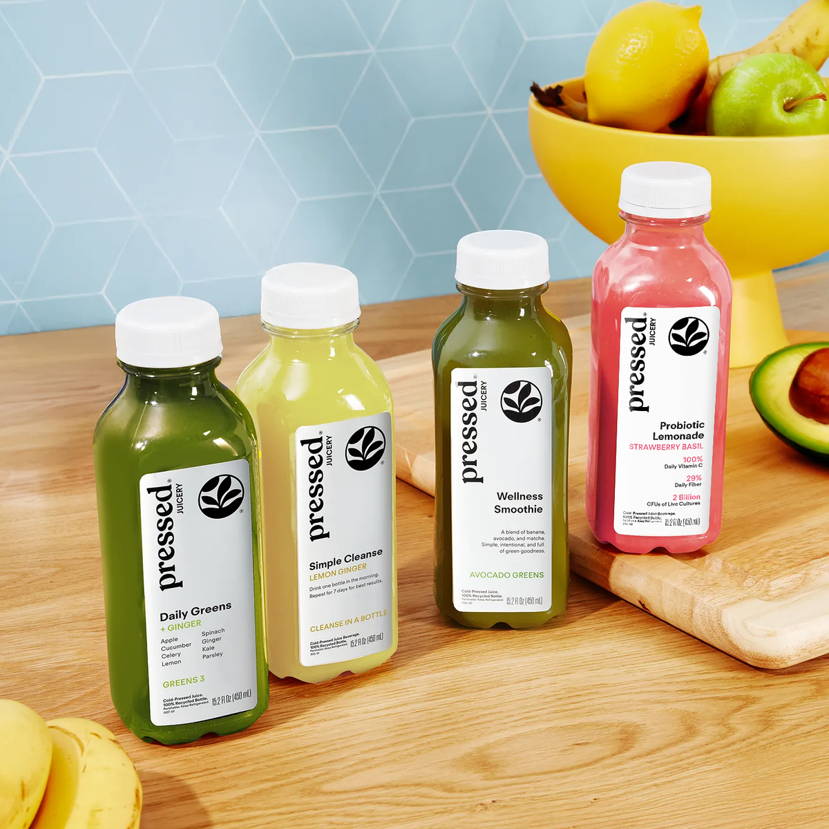 Bottles of 'pressed' juice on a wooden table with fruits in the background